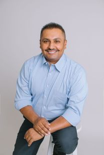 Smiling man in a light blue shirt seated against a plain gray background