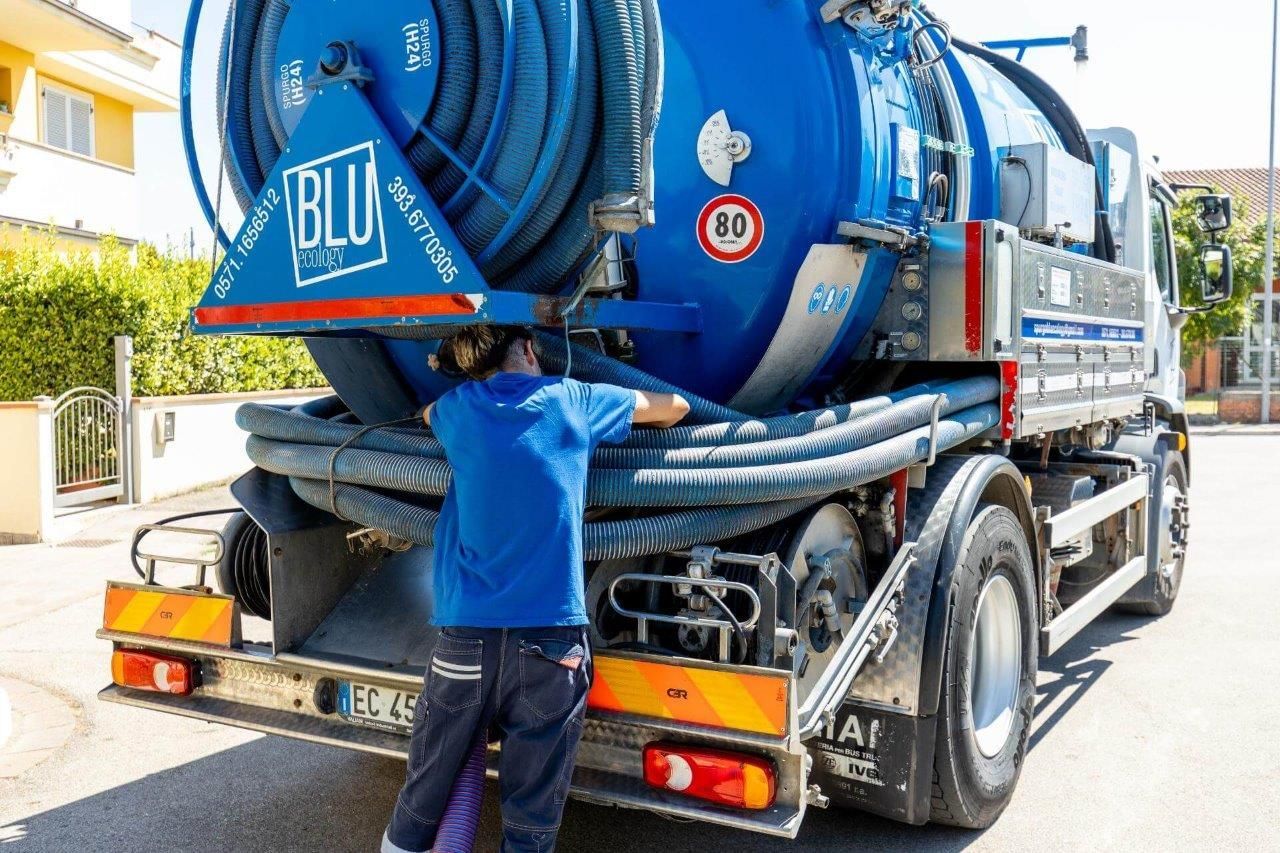 Una persona vestita di blu lavora su un grande camion della nettezza urbana blu e bianco.