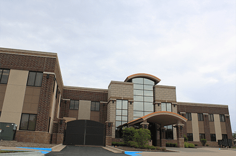 A two-story commercial building featuring brick and stone facade, a glass-enclosed entrance, and a paved parking lot.