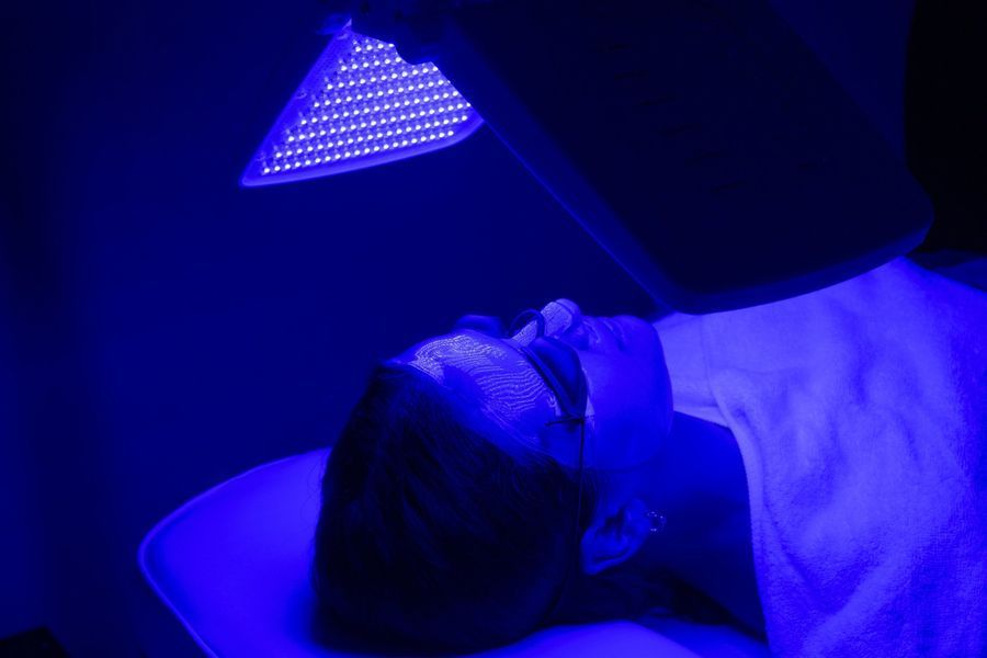 A person lies on a treatment table undergoing blue light therapy, wearing protective eye goggles.