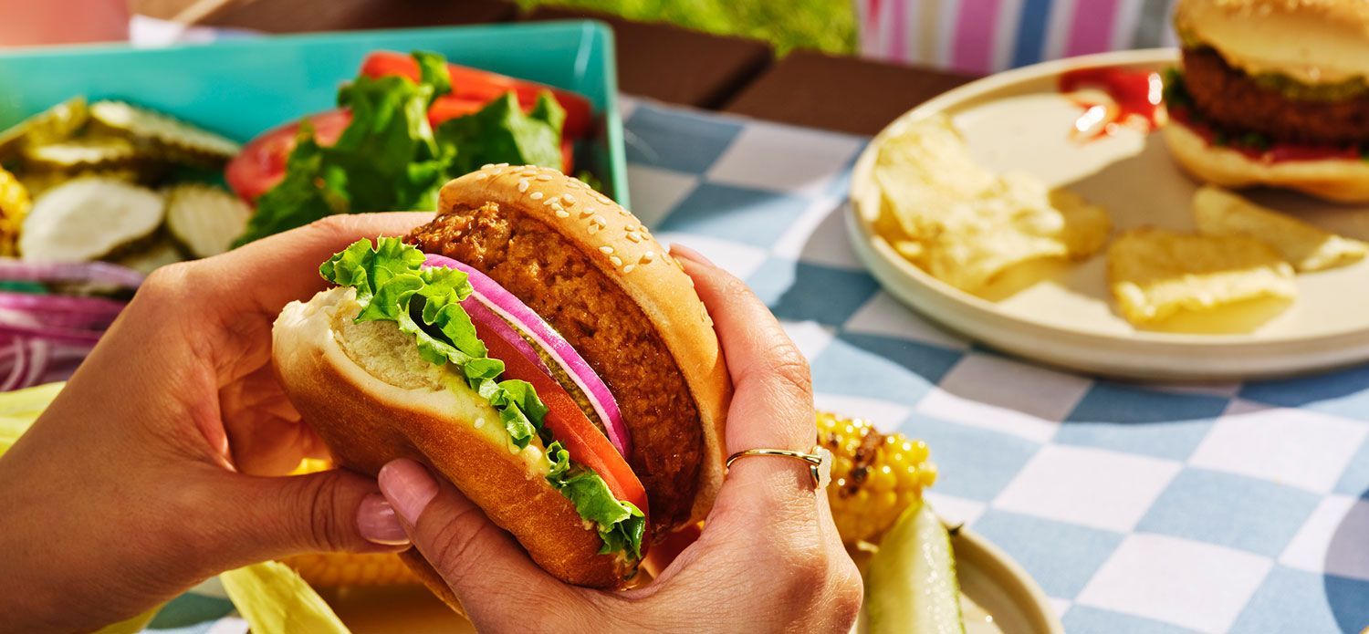 Image of hands holding Dr. Praeger's burger in an outdoor picnic setting