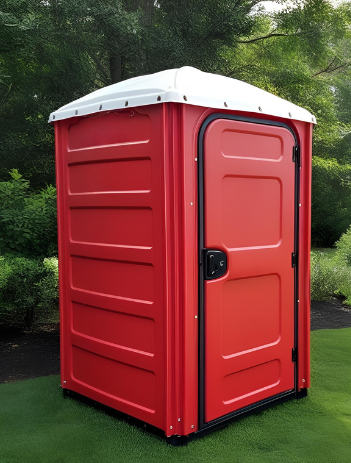 A red portable toilet is sitting on top of a lush green field.
