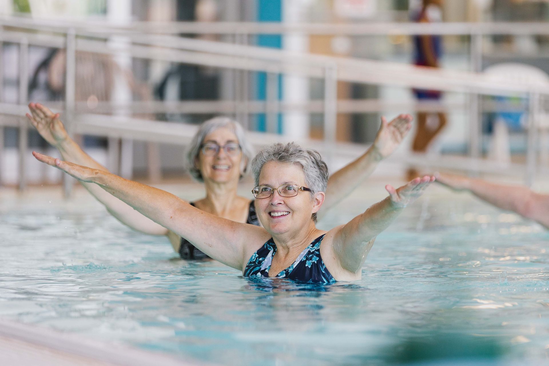 Two older women are doing aerobics in a swimming pool.