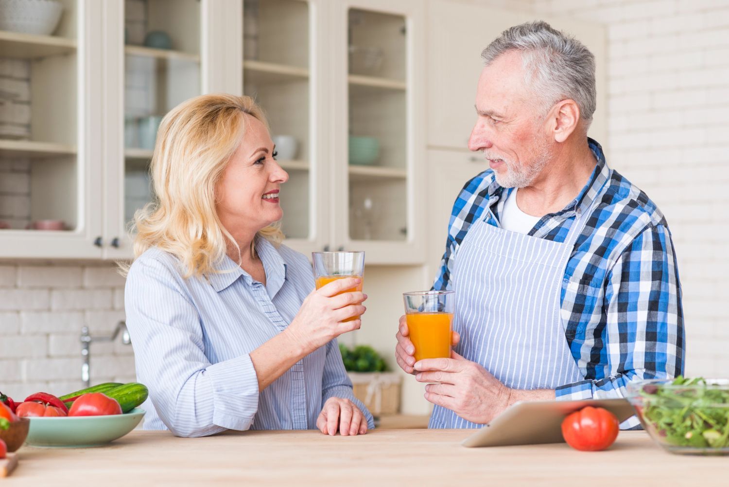 A man and a woman are drinking orange juice in a kitchen.