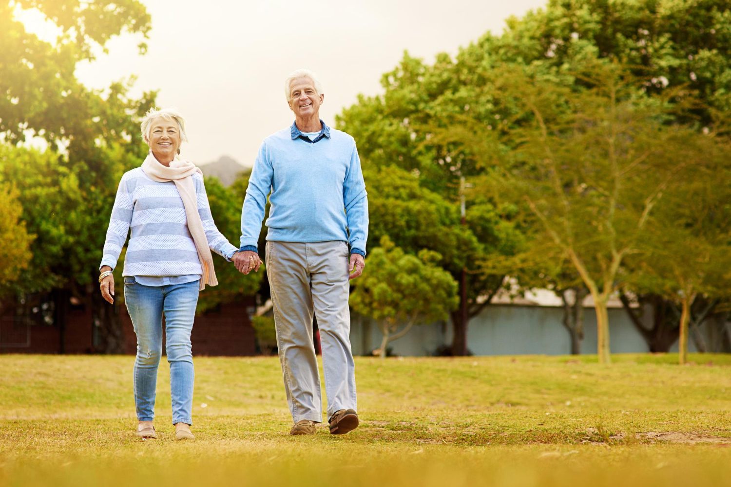 An elderly couple is walking in a park holding hands.
