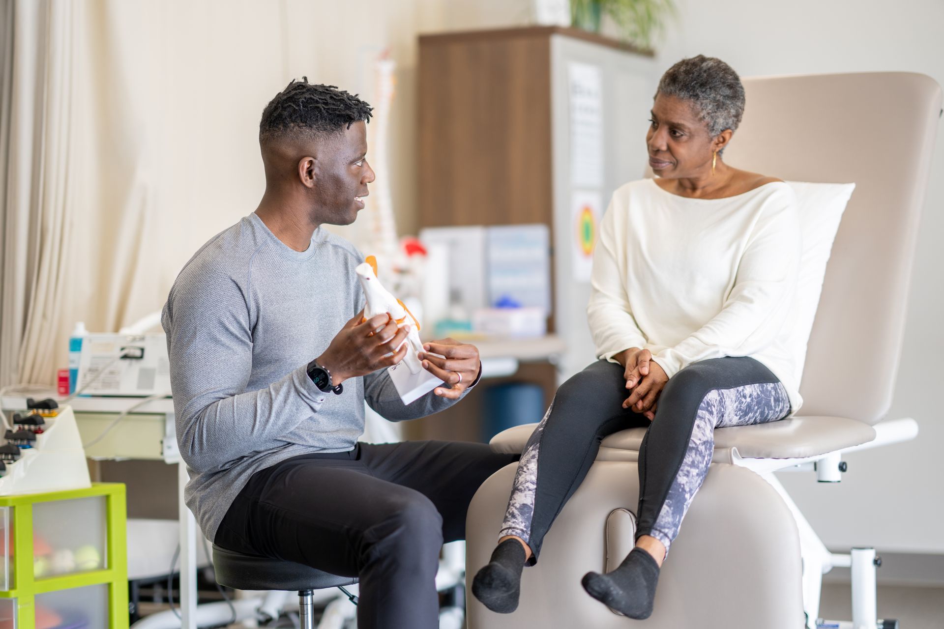 A man is talking to a woman sitting on a chair in a doctor 's office.