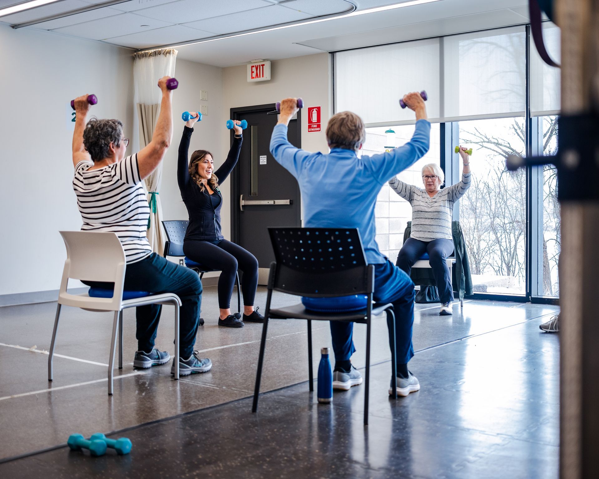 A group of people are sitting in chairs and lifting dumbbells in a gym.