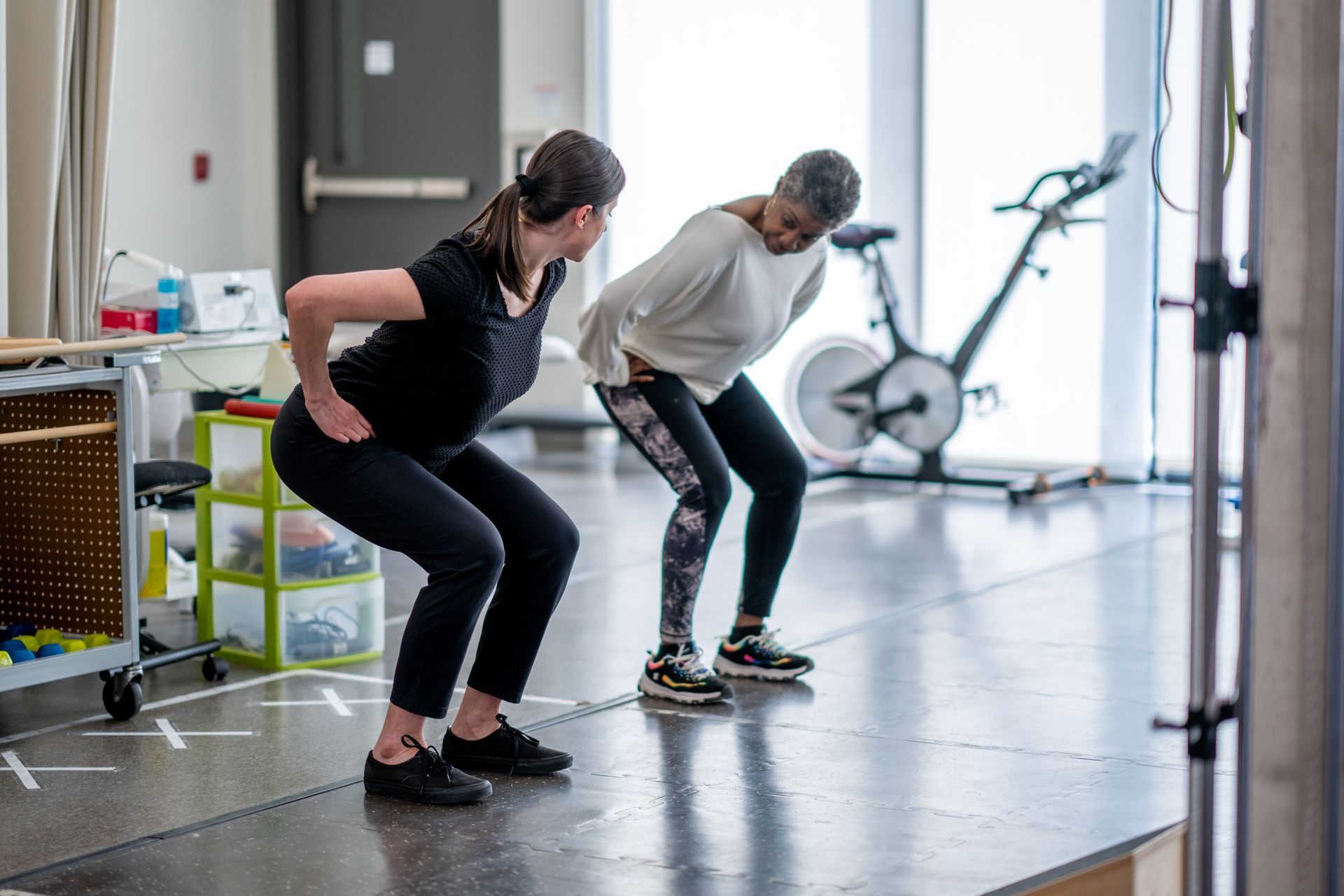 Two women are squatting next to each other in a gym.