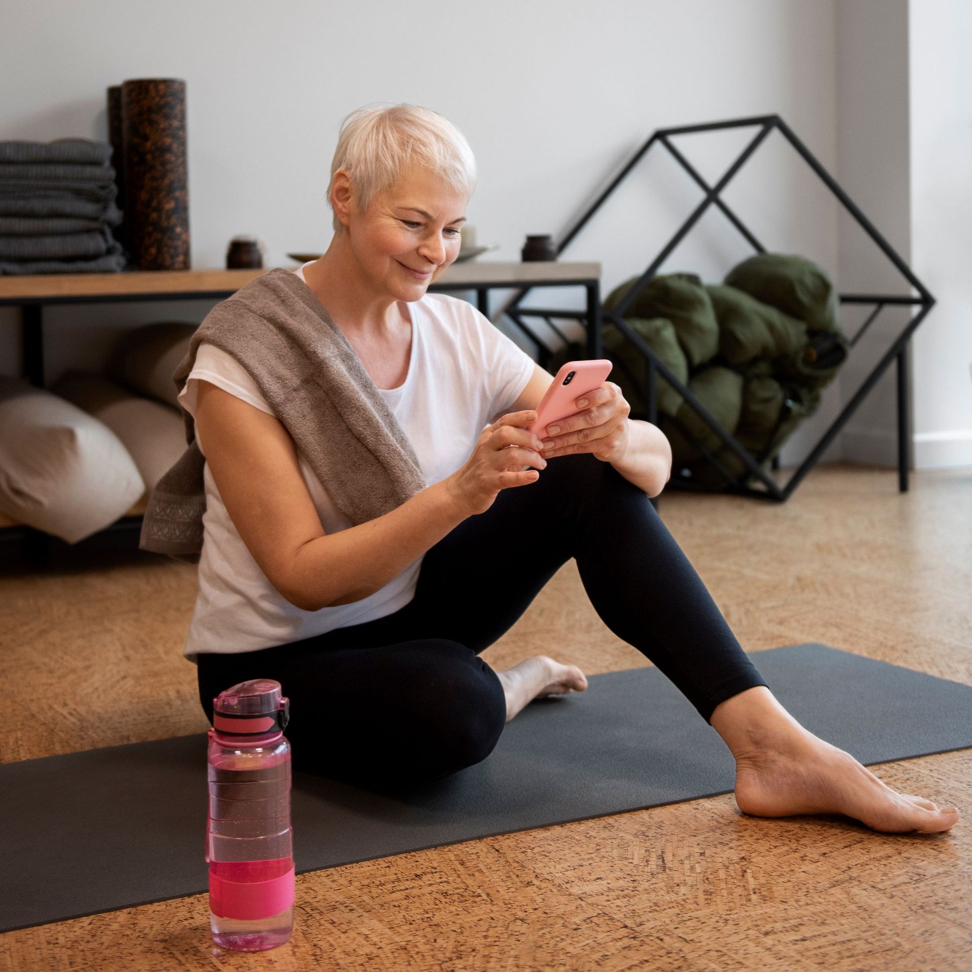 A woman is sitting on a yoga mat looking at her phone