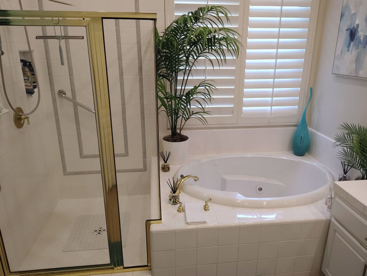 Bathroom with glass shower, white soaking tub, plants, and gold fixtures in a bright, tiled room