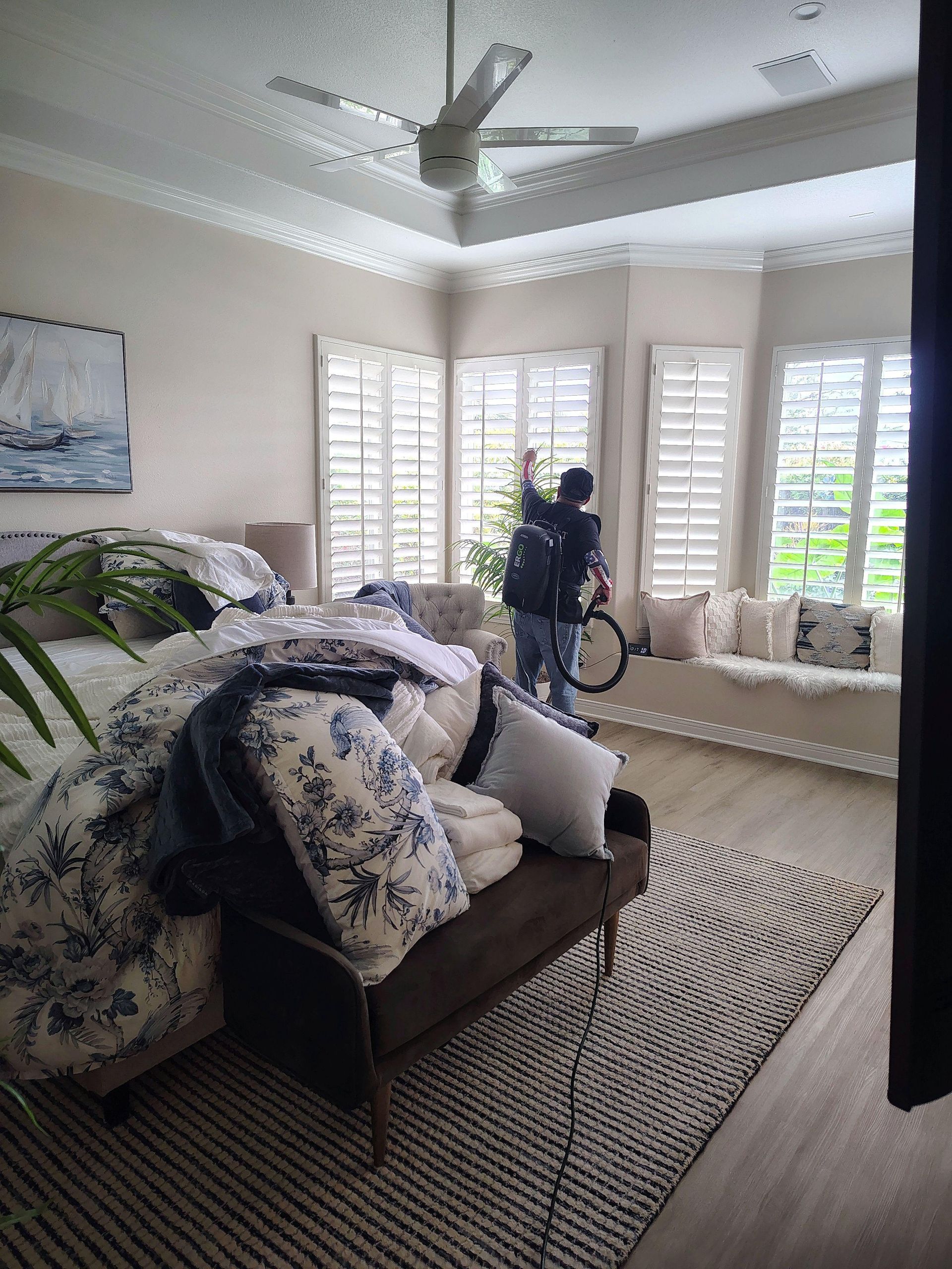 Bright living room with patterned sofa, large windows, ceiling fan, and person by the window.
