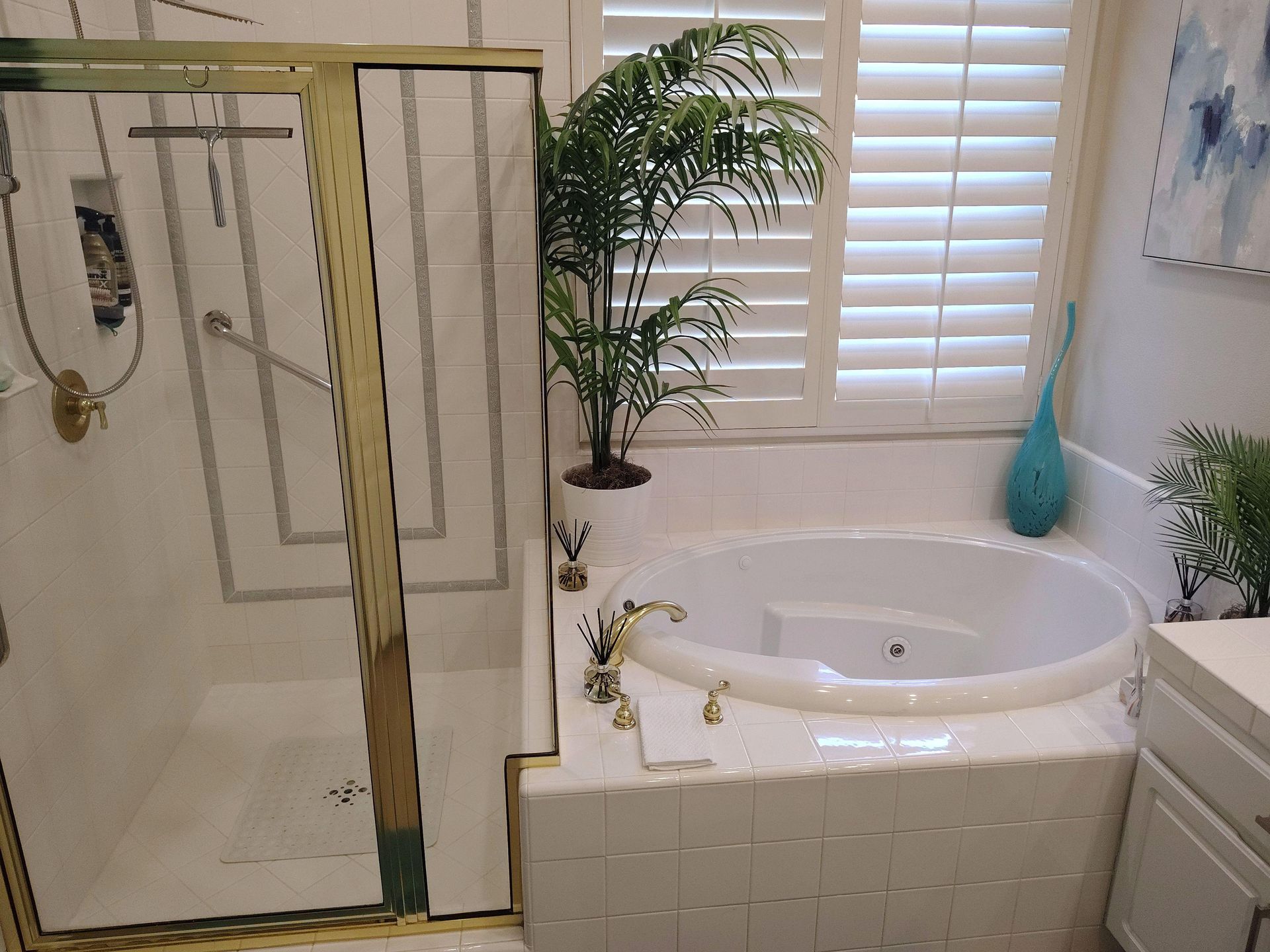 Bathroom with glass shower, corner soaking tub, white tile, plant, and window shutters.