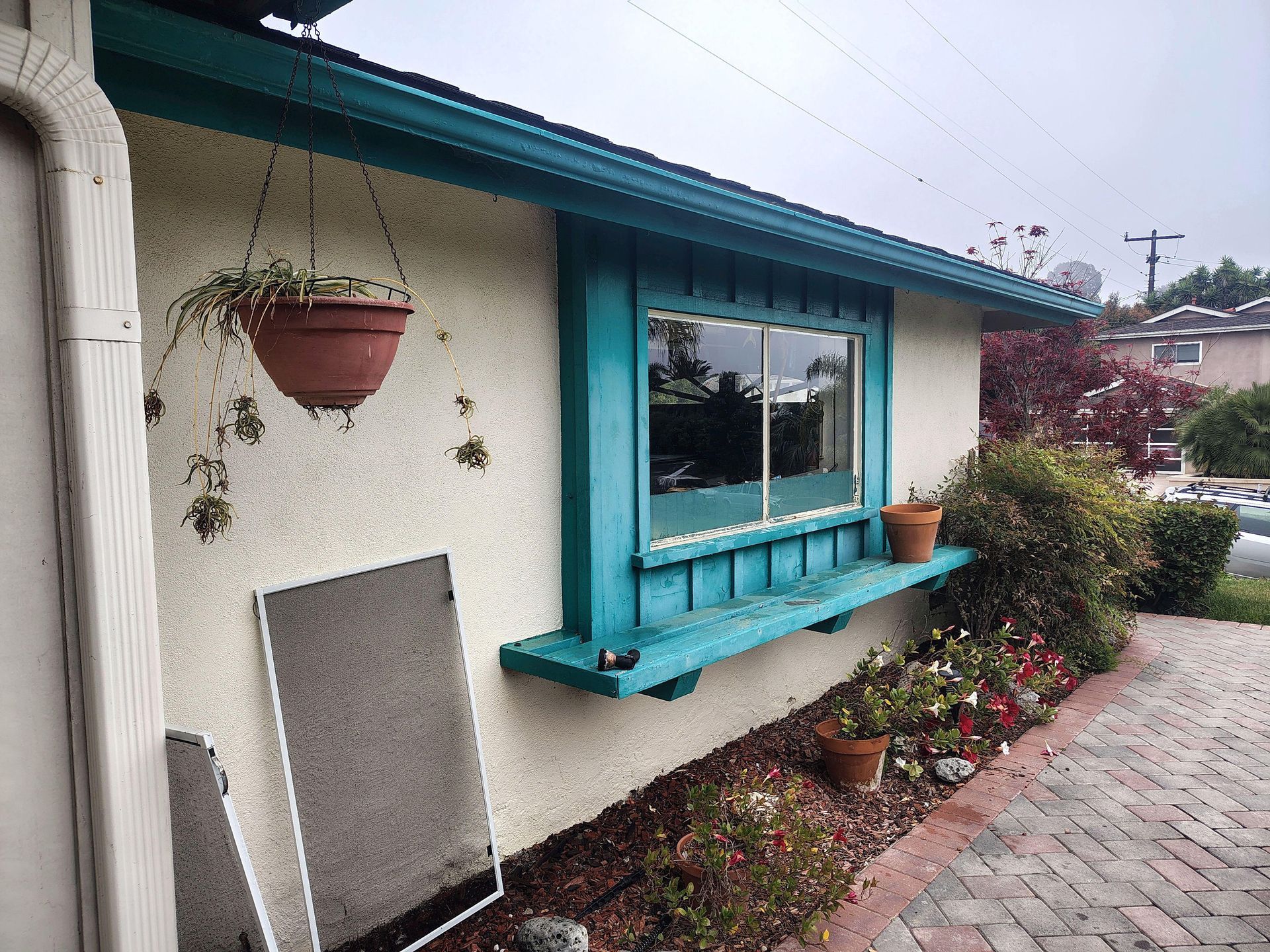 Turquoise house exterior with hanging planter, window box, and brick walkway beside a garden path
