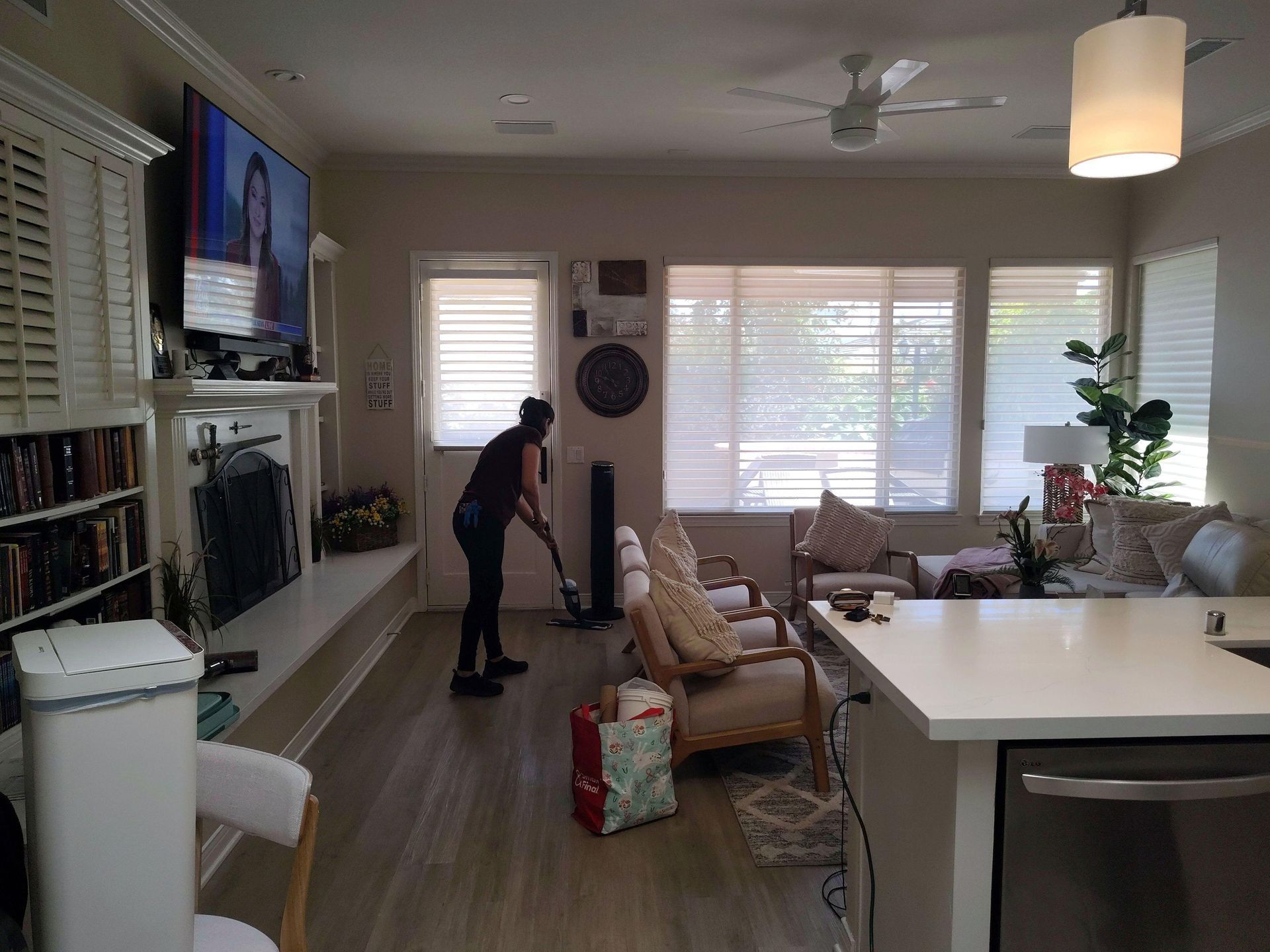 Person vacuuming a bright living room with wall-mounted TV and large windows