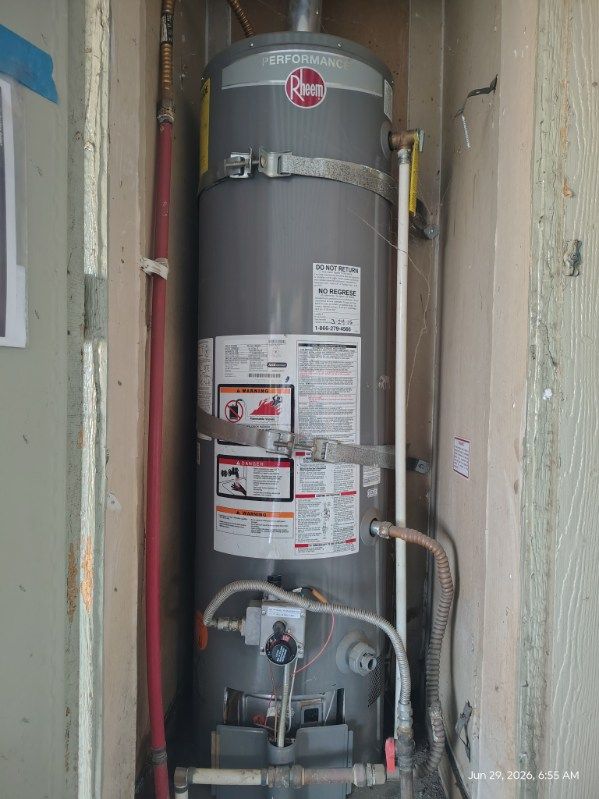 Water heater in a narrow utility closet with visible pipes, valves, and warning labels.