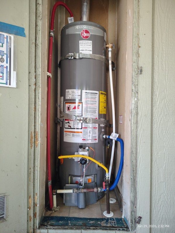 Water heater in a narrow utility closet with red and blue pipes and labels on the tank.