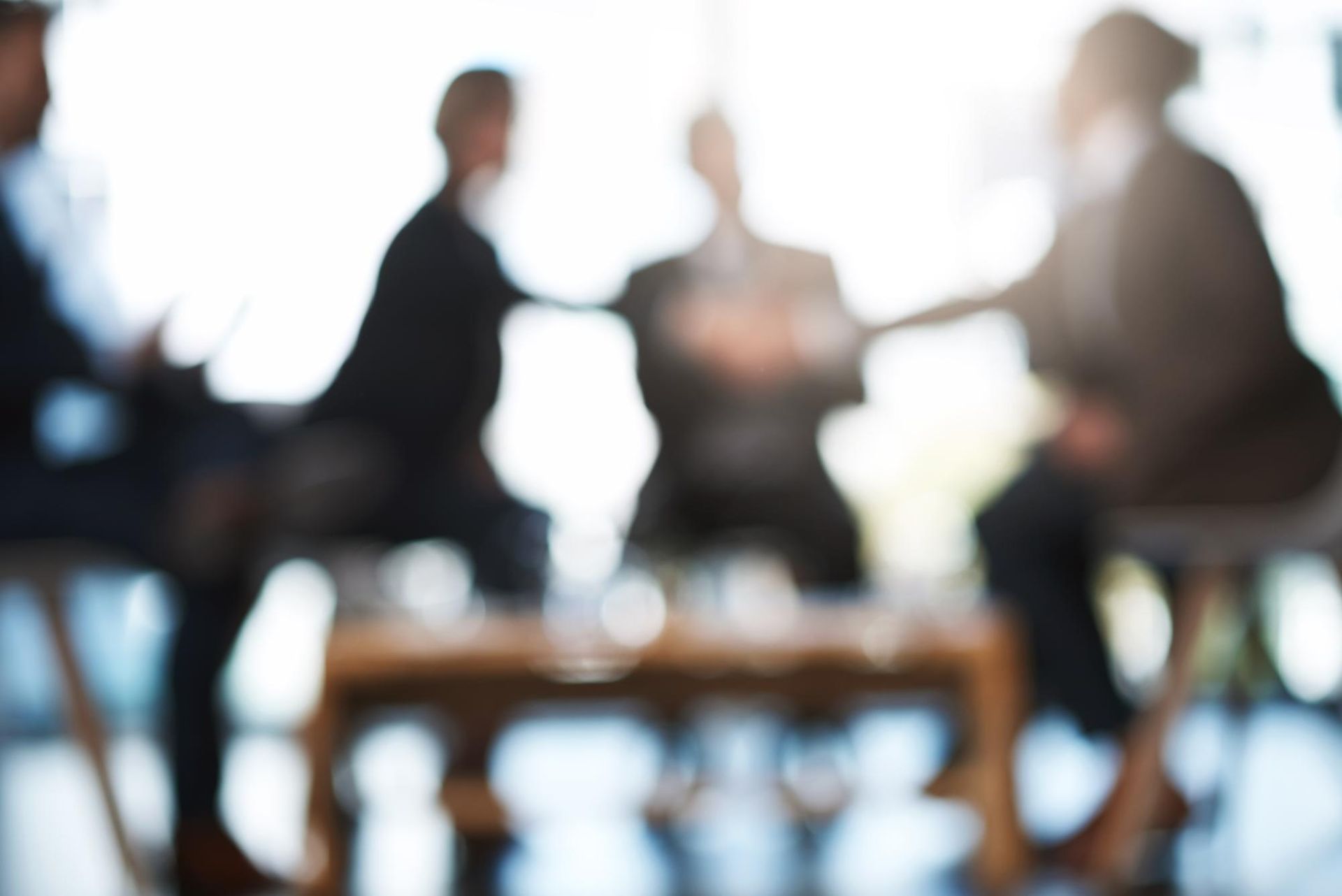 Blurred view of a business meeting. People seated around a table, possibly discussing ideas in an office.