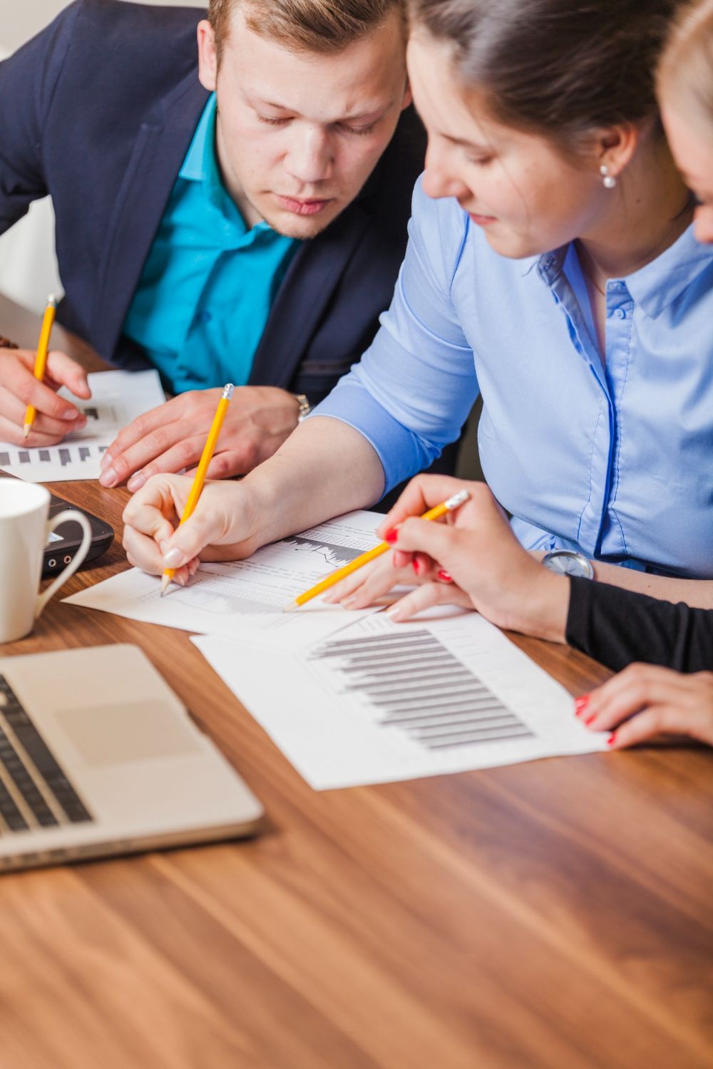 Three colleagues reviewing documents with a laptop and coffee mug on a wood table.