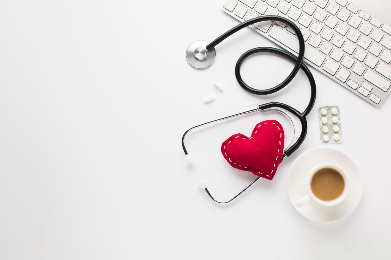 Stethoscope, red heart, pills, keyboard, and coffee cup on a white background, symbolizing healthcare and wellness.