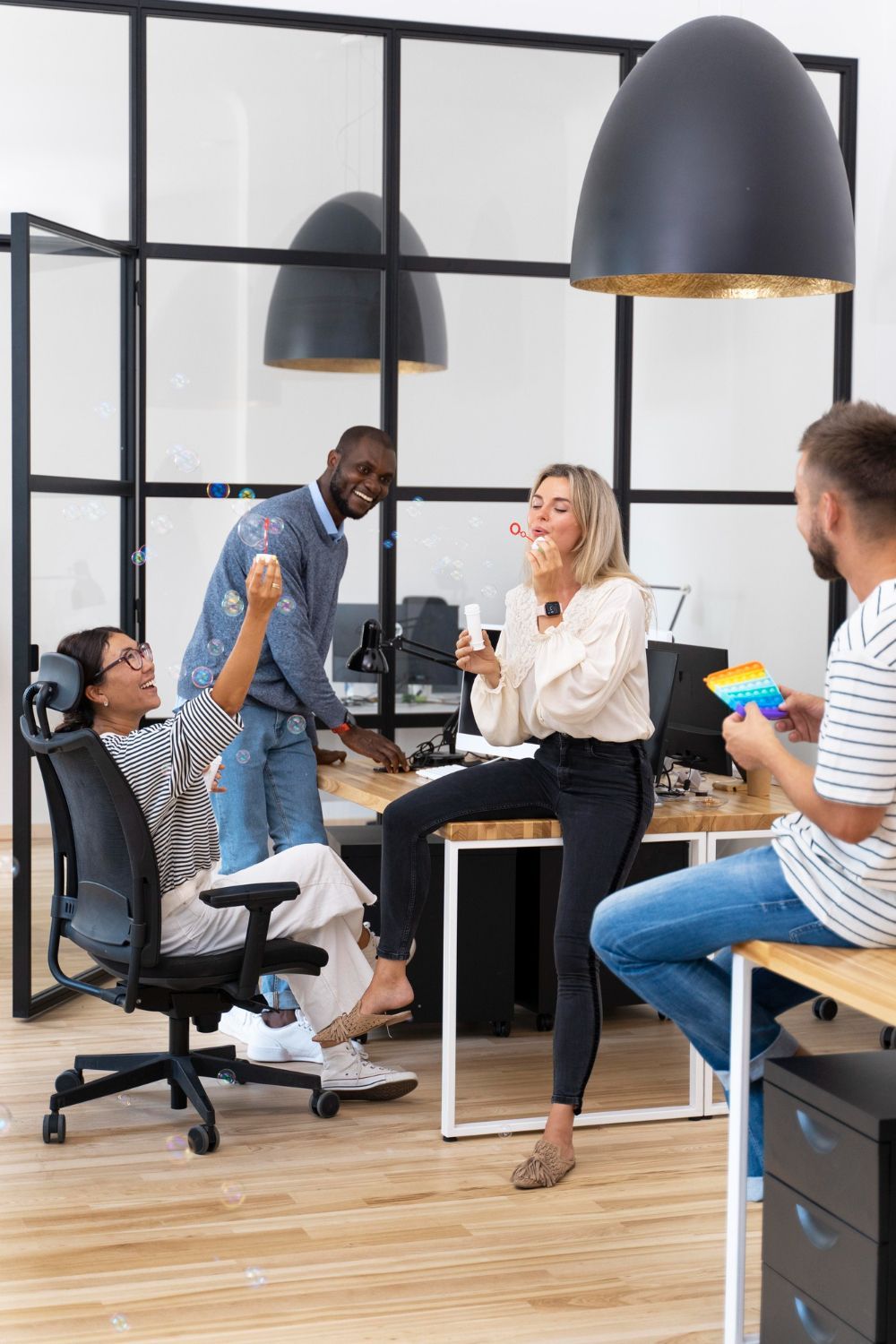 Four people in a modern office: two sitting and two standing, interacting near desks.