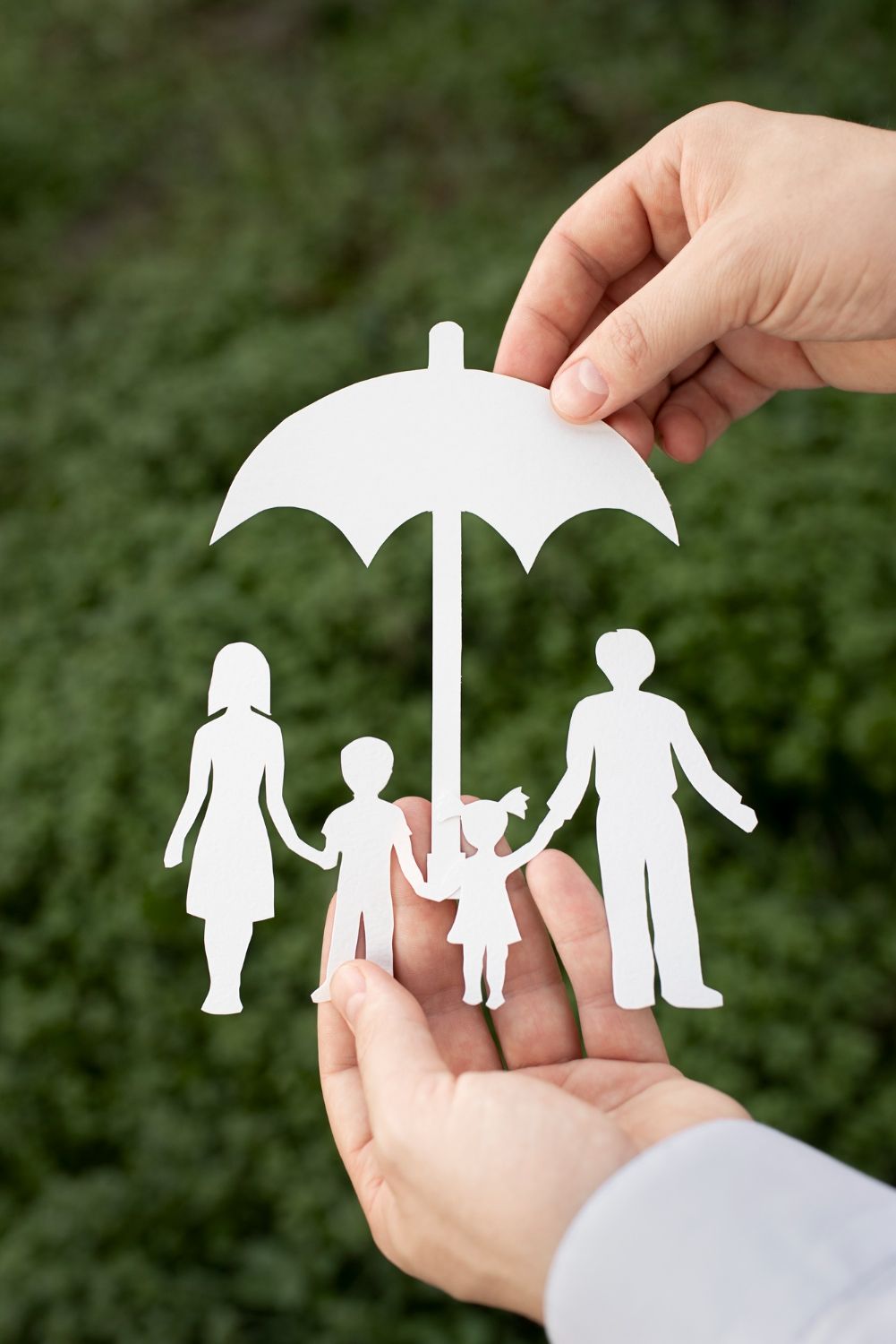 Hands holding a paper cutout of a family under an umbrella, against a green background.