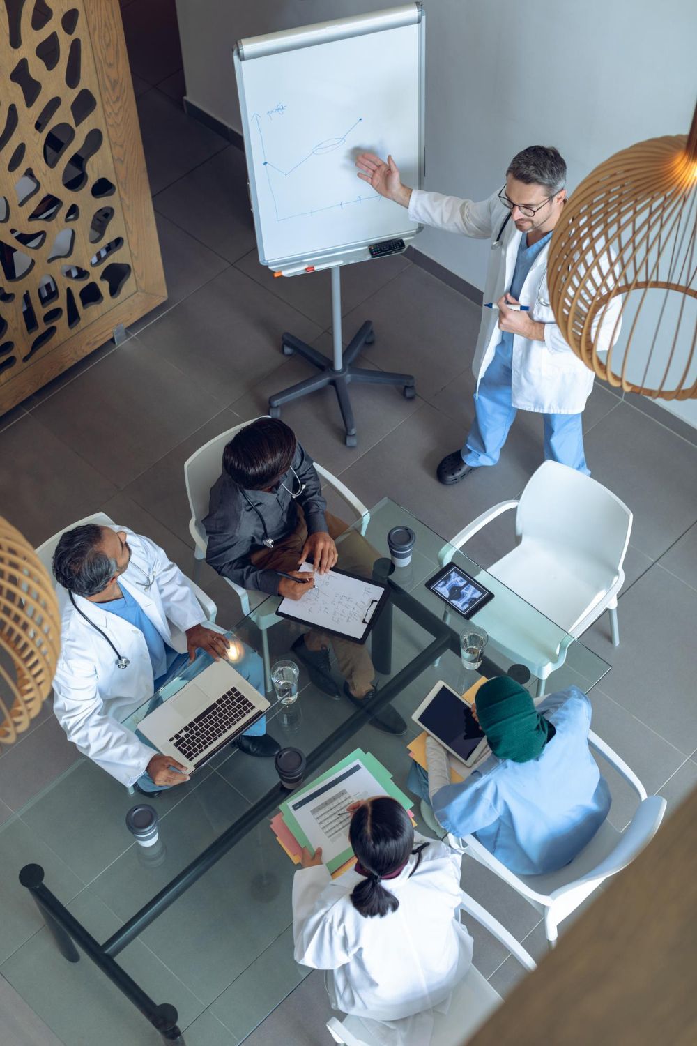 Medical team in meeting with one doctor pointing at whiteboard.