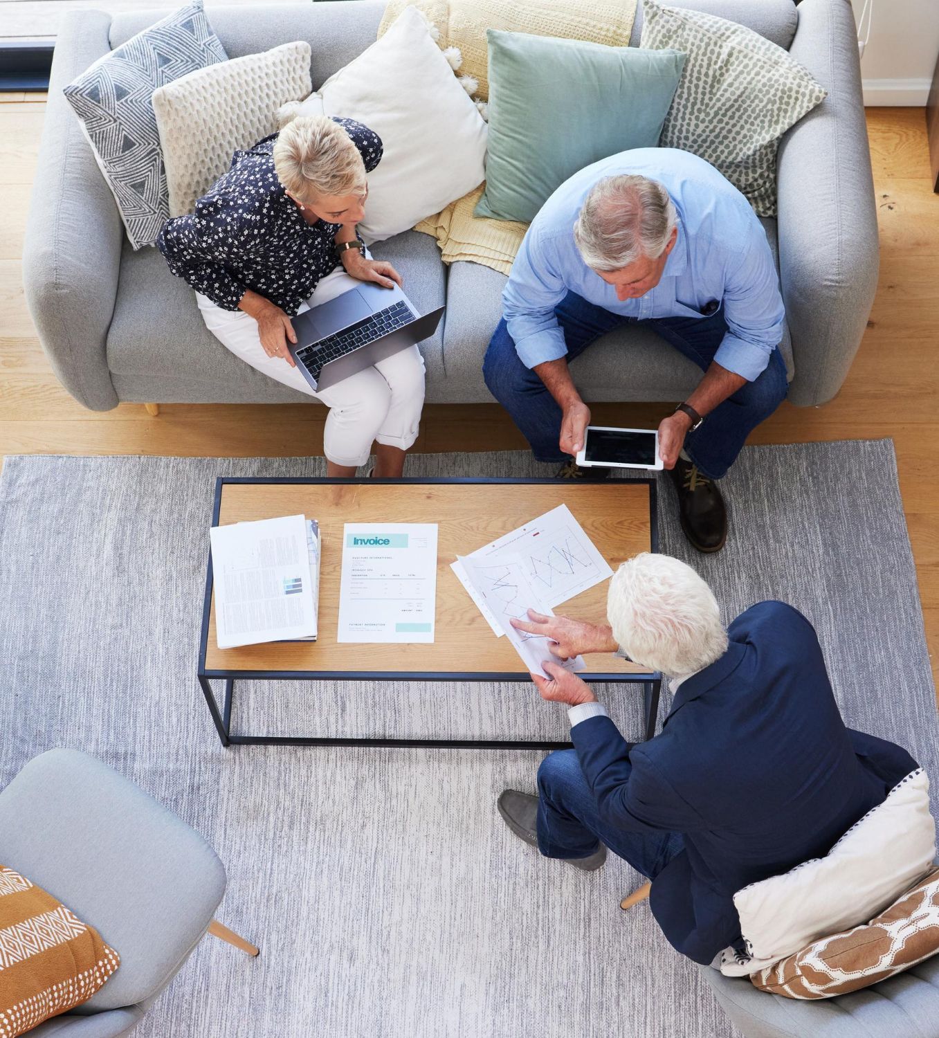 Overhead view: Couple on couch, advisor at coffee table, reviewing documents.