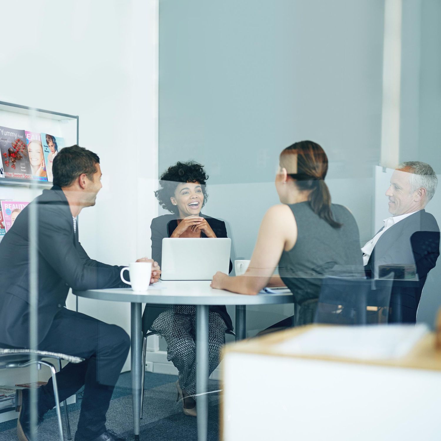 Group of people in a meeting, around a small table in a modern office, smiling and discussing.