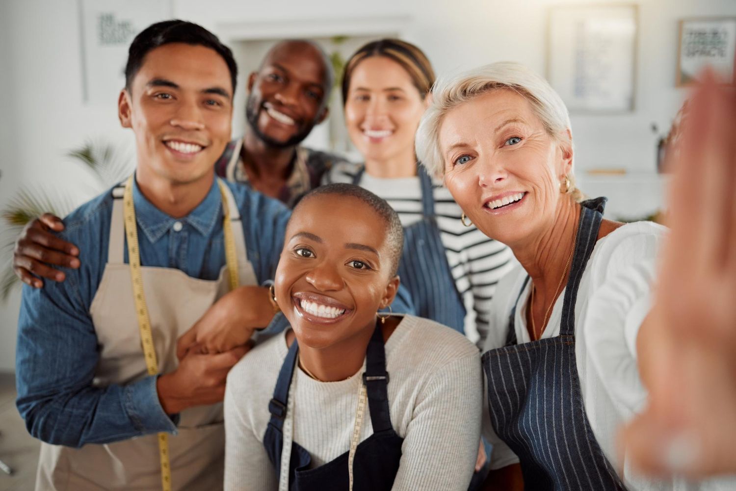 Group of five smiling people, some wearing aprons, in a brightly lit setting, possibly a workshop.