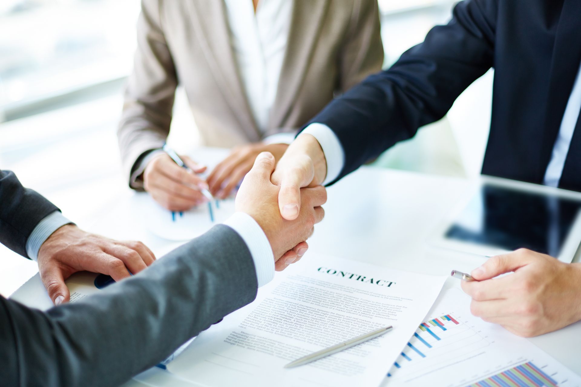 Businesspeople shaking hands over a contract at a table.