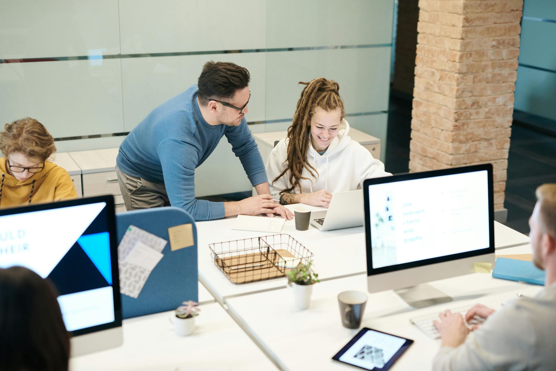 People working collaboratively at office desks with computers. A woman smiles while looking at a laptop.