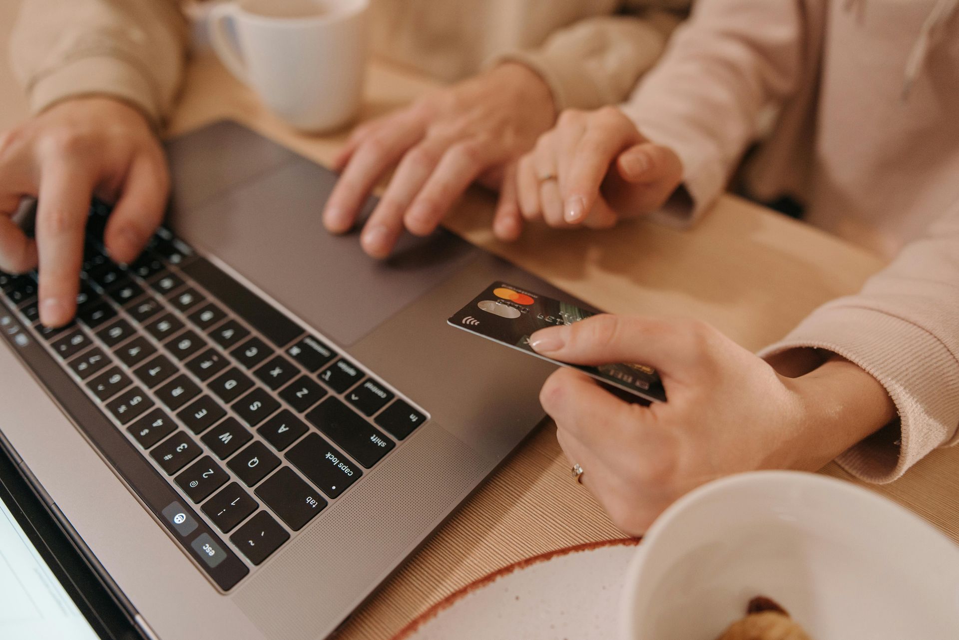 Hands typing on a laptop and holding a credit card on a table.