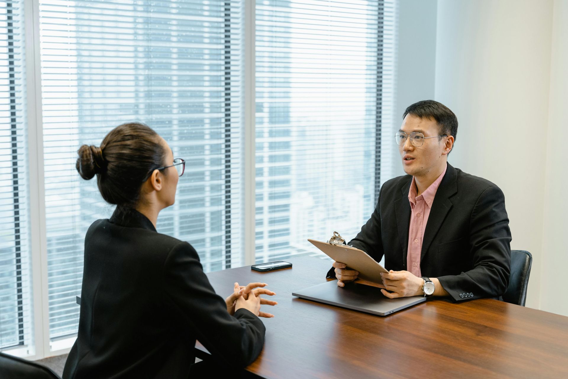 Man in suit interviewing woman at a table; they are in an office setting.
