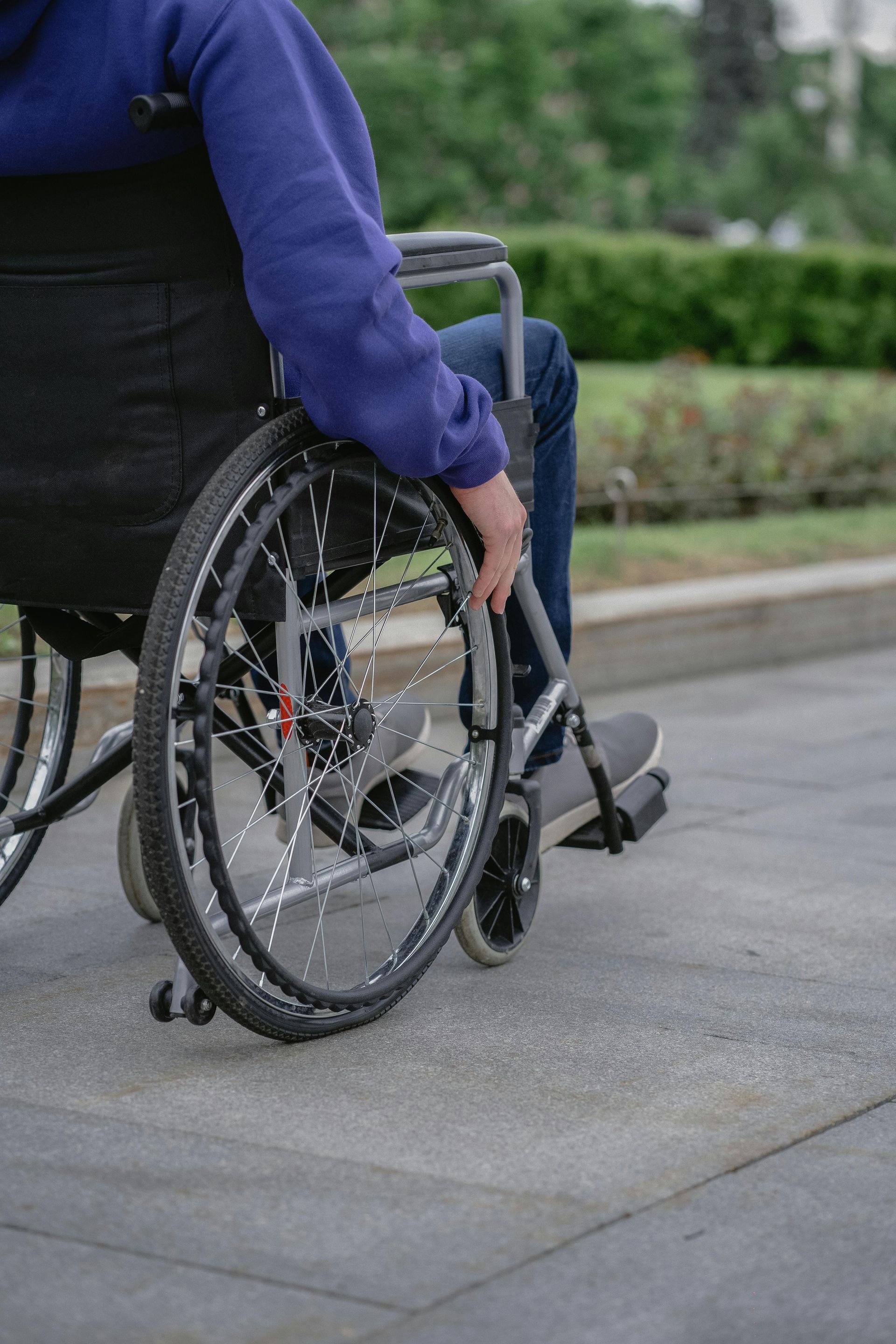 Person in a wheelchair on a paved path, hand on the wheel.