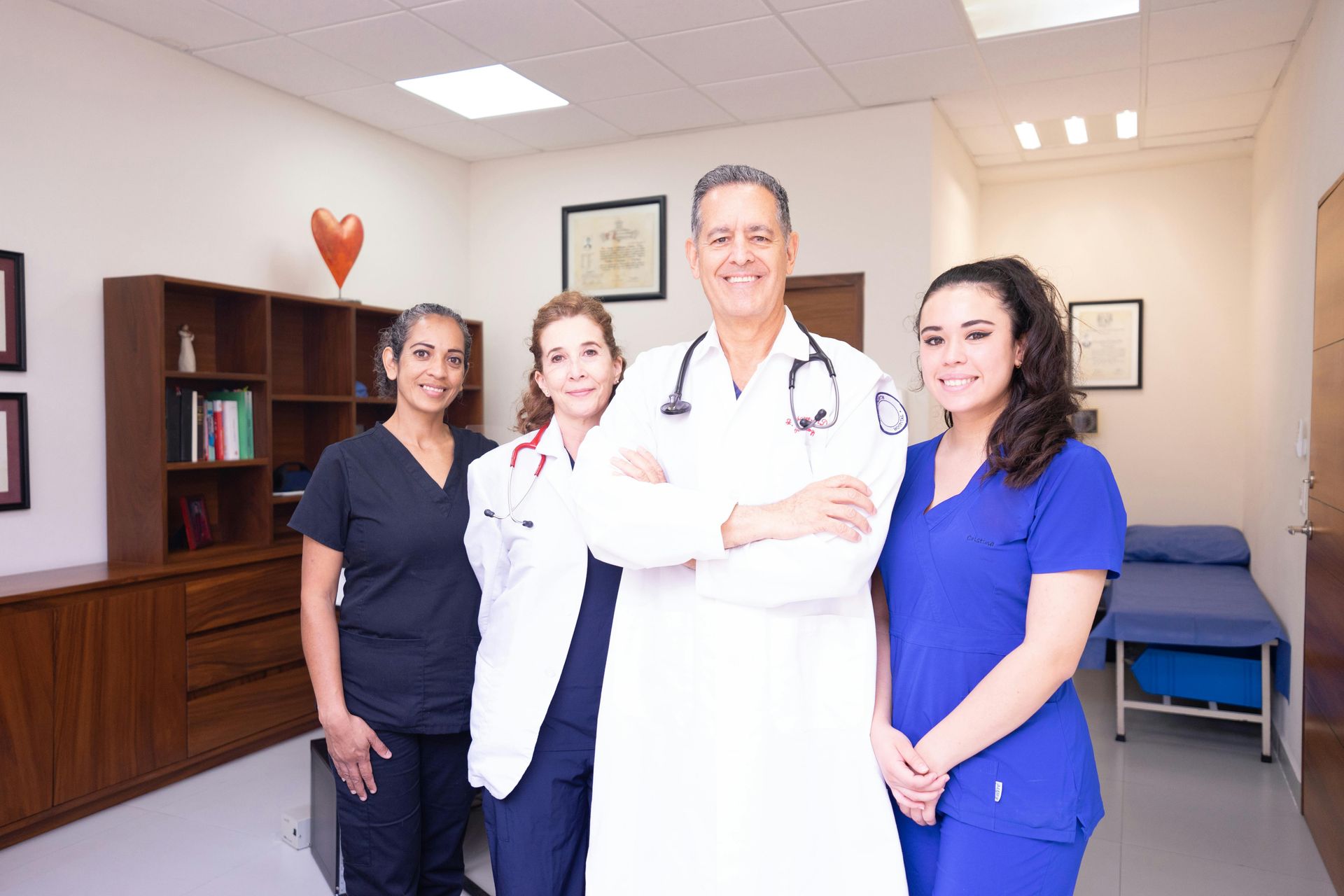 Medical team in a doctor's office: doctor in white coat with arms crossed, three staff members.