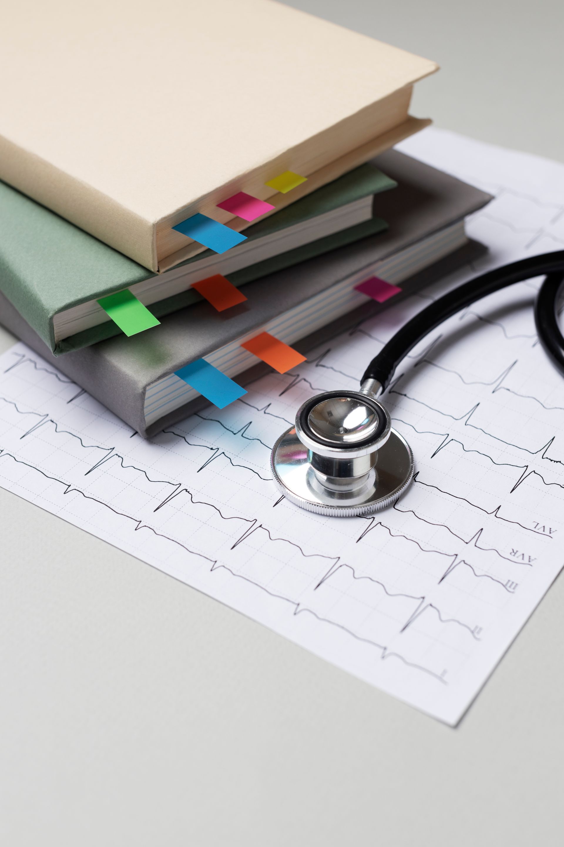 Books with sticky notes and stethoscope on electrocardiogram.