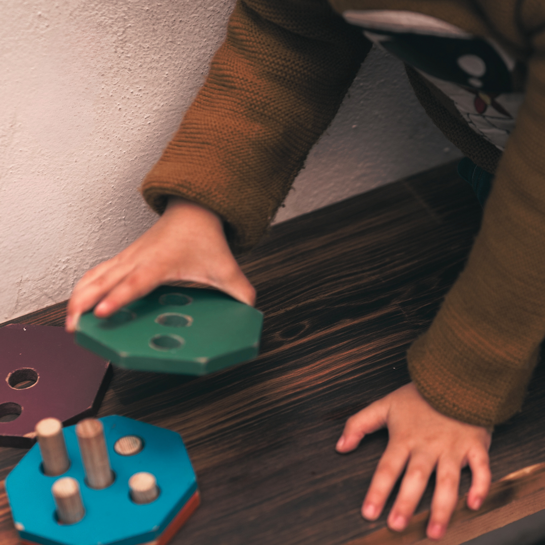 Child playing with colorful wooden shapes on the floor near a wall