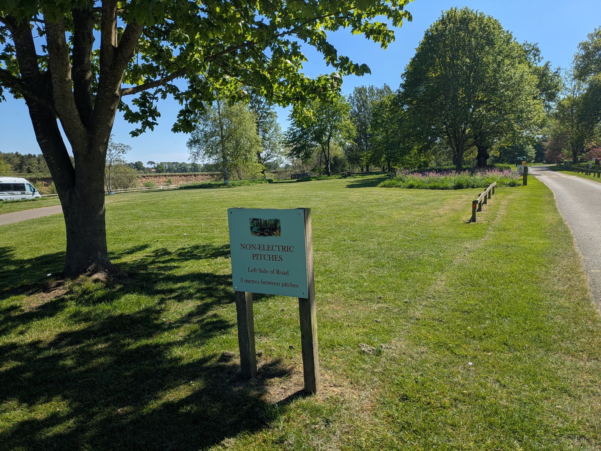 Asphalt road leads past grassy field and trees. A red utility box stands in the distance.