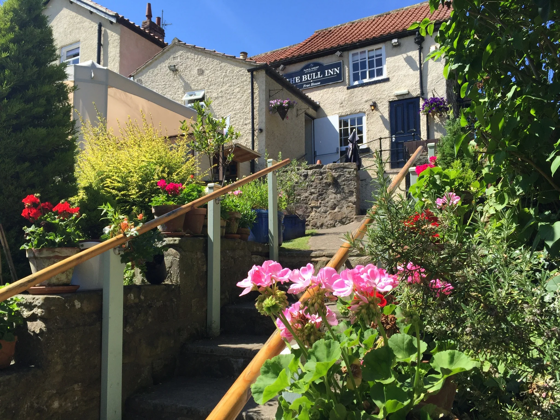 Stone steps leading up to a cottage with flowers, a handrail, and a pub sign.