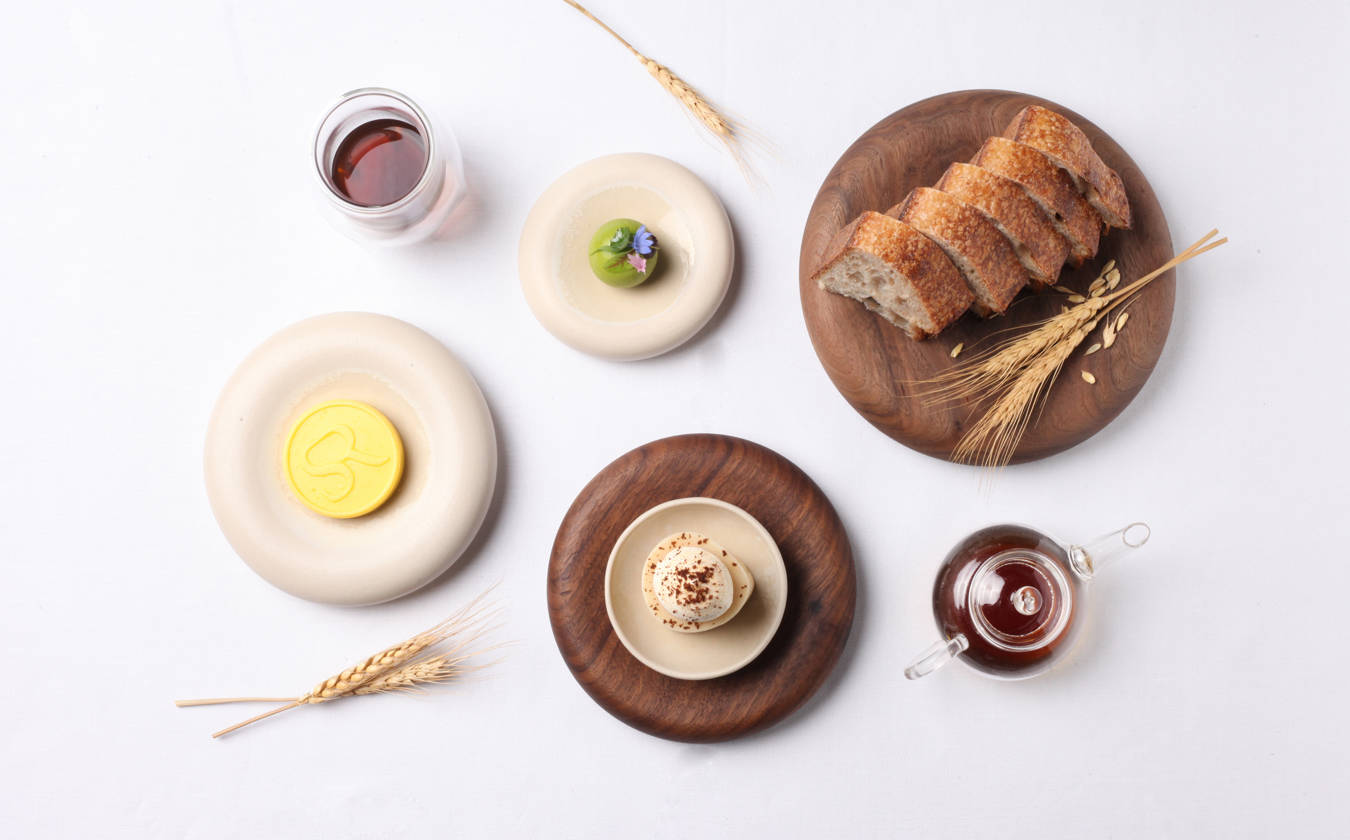 Overhead shot of various gourmet foods on plates and wooden boards, including bread, butter, and sauces.