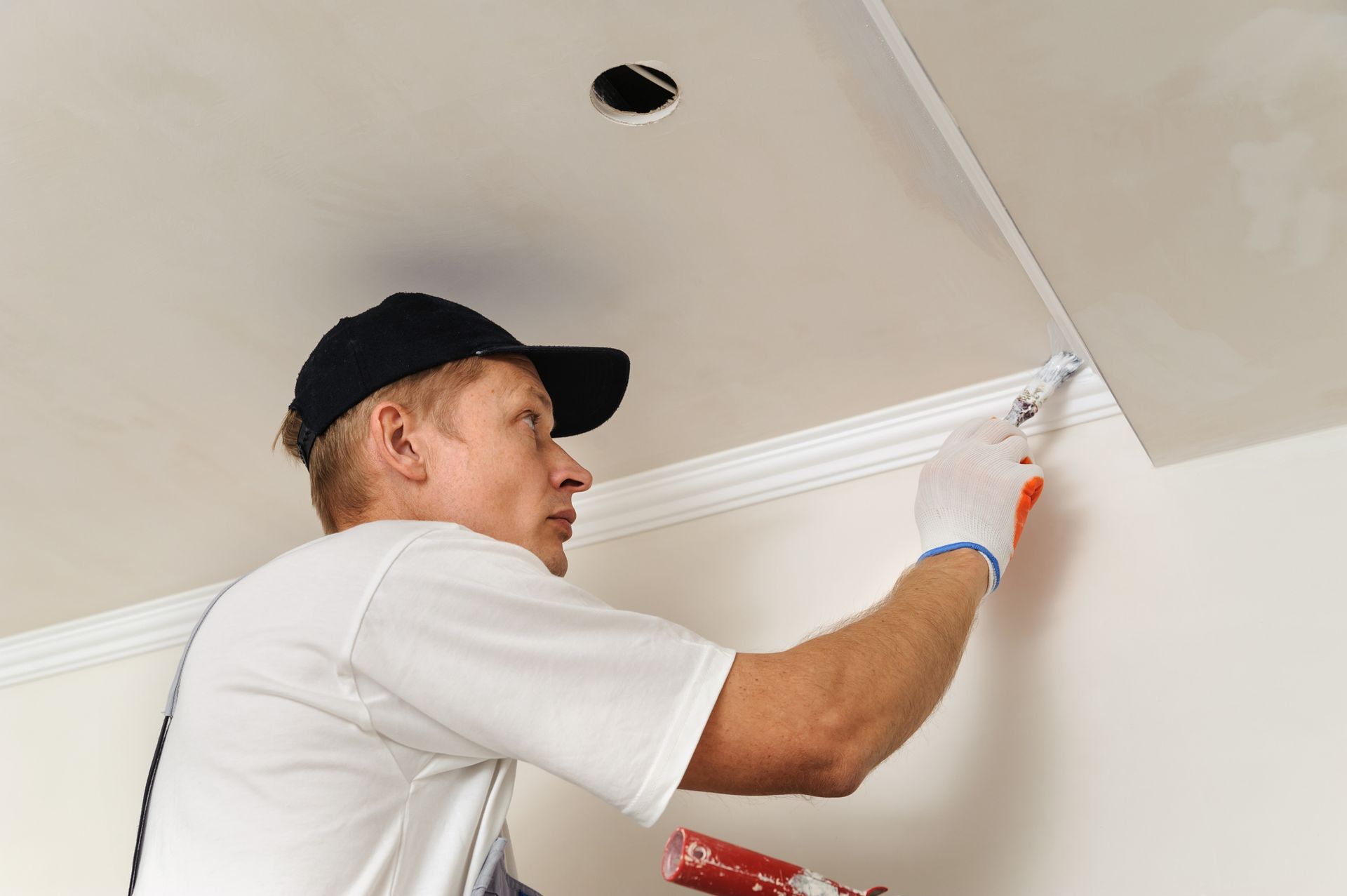 A man is painting the ceiling of a room with a paint roller.
