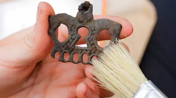 Una mano sostiene un objeto decorativo de metal polvoriento mientras se le quitan los residuos con un cepillo suave.
