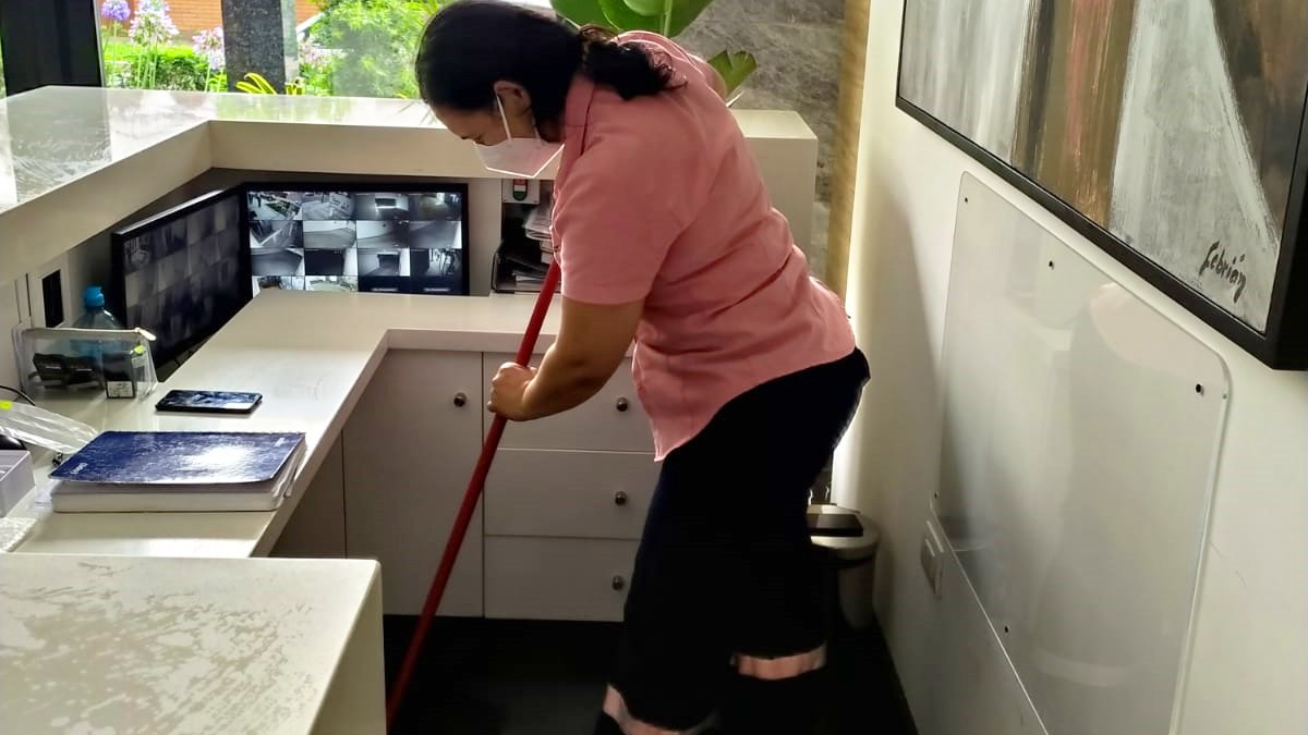 Una persona está fregando el suelo blanco de una oficina cerca de un escritorio y armarios de pared.