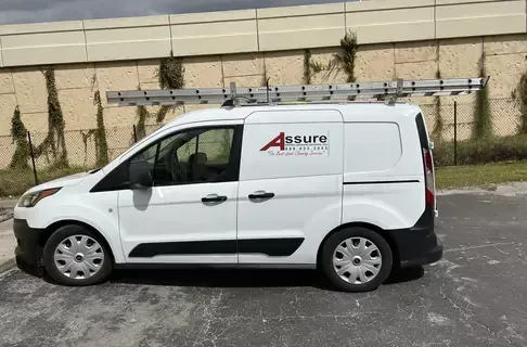 A white van with a ladder on top of it is parked in front of a building.