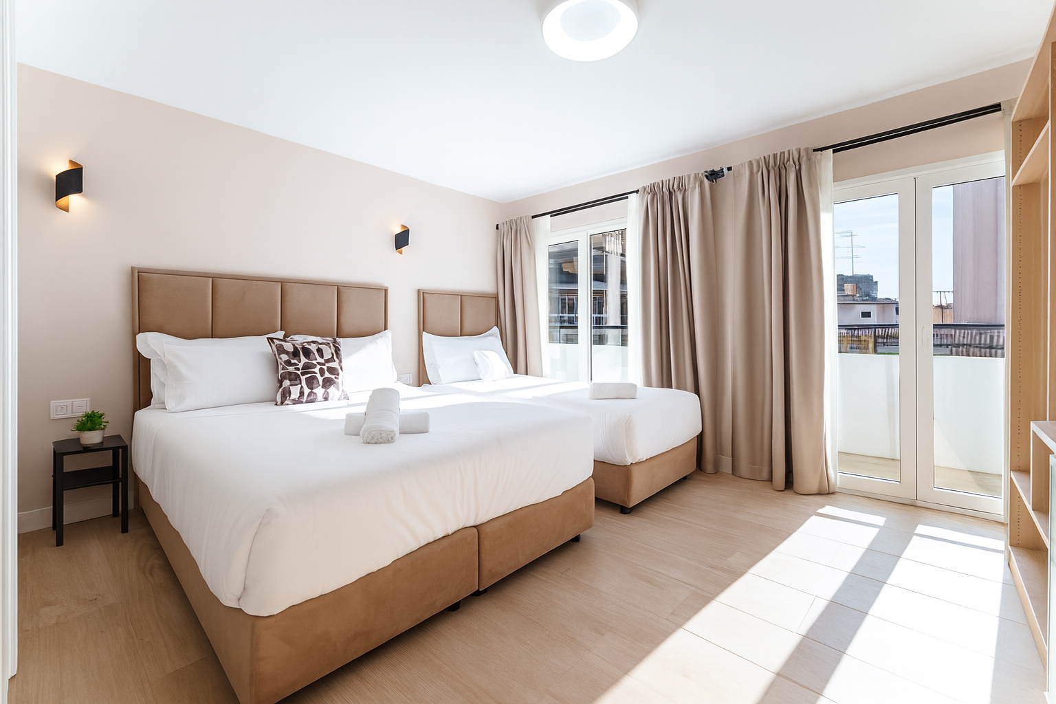 Dormitorio con dos camas, paredes color beige, grandes ventanas y balcón.