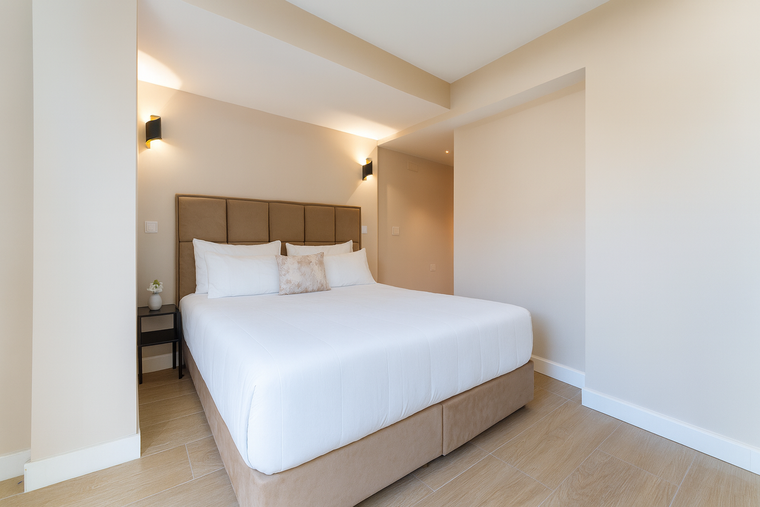 Dormitorio con cama, mesita de noche y apliques de pared. Paredes color beige, suelo de imitación madera clara,moderno