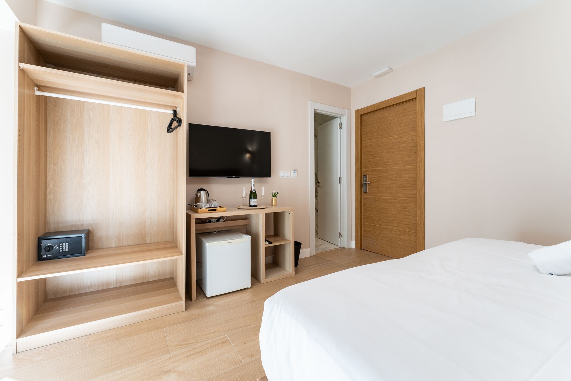 Habitación de hotel con cama, TV, mininevera, armario y puerta cerrada.