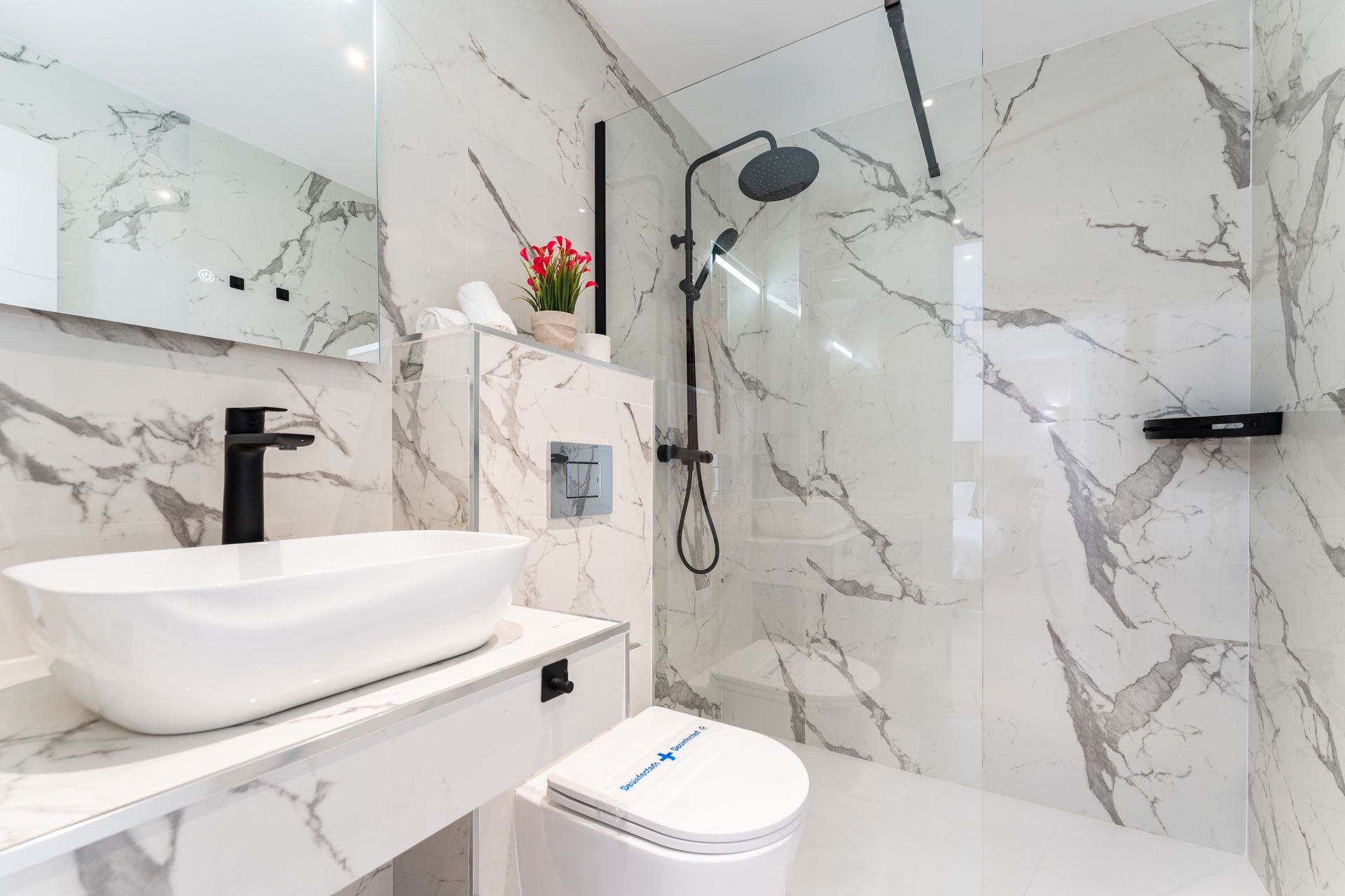 Baño moderno con paredes de mármol blanco, lavabo blanco y grifería negra.