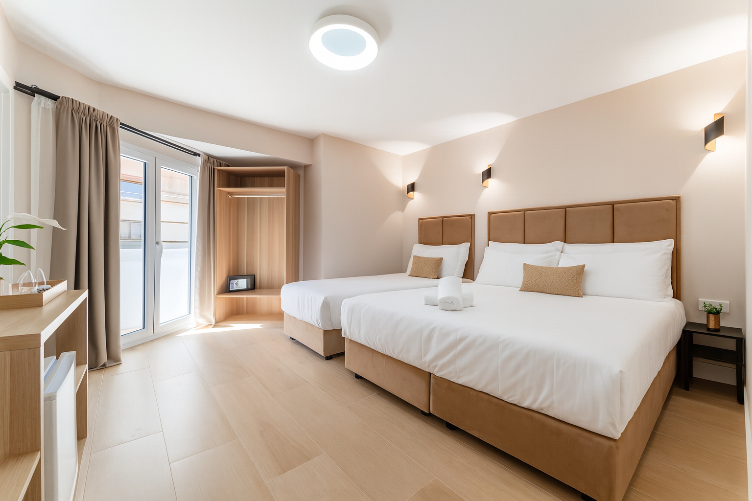 Habitación de hotel con dos camas, balcón abierto, suelo de madera clara, colores neutros.