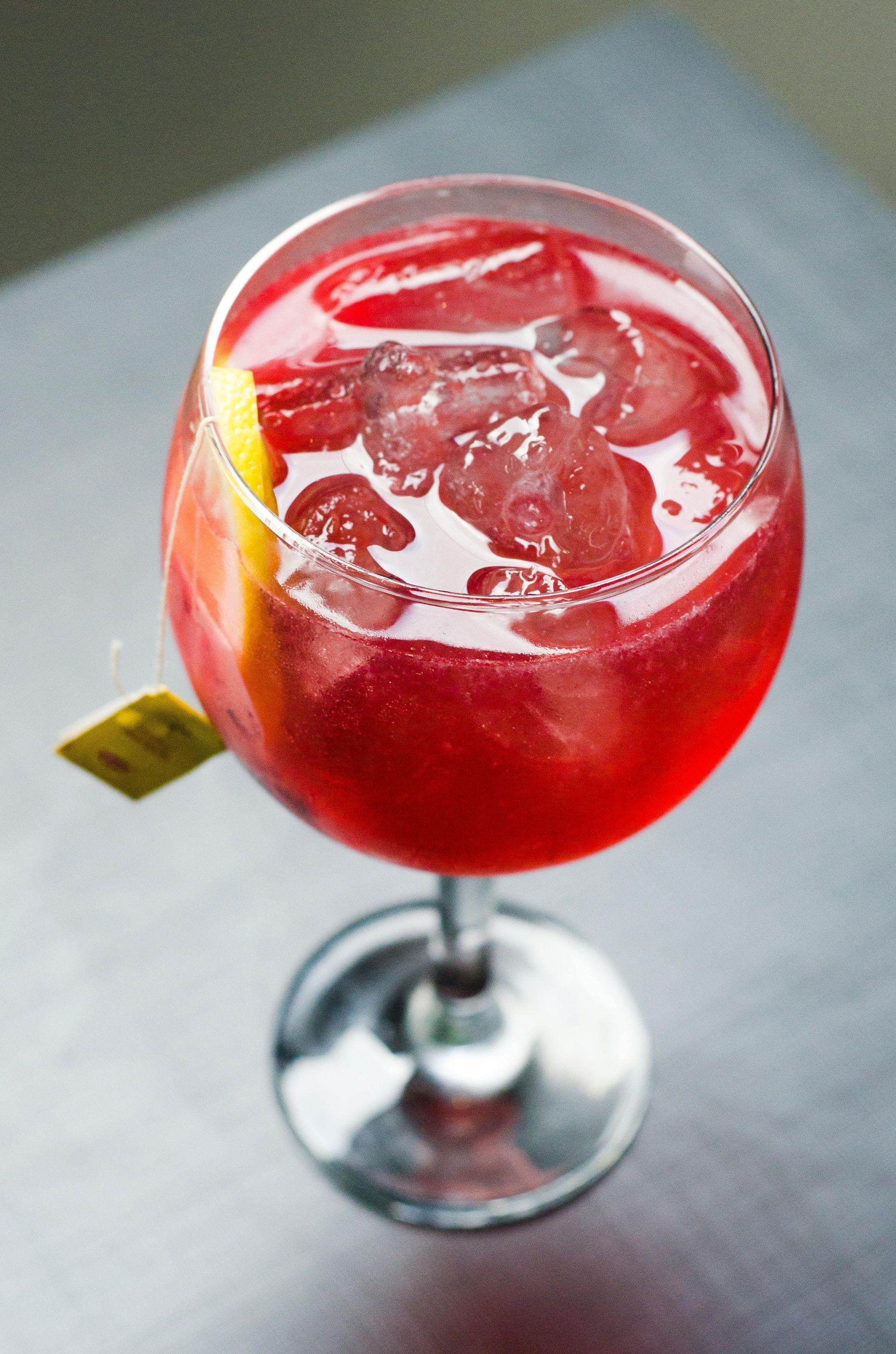 Cóctel rojo servido en copa con pie, con hielo y una rodaja de limón como adorno.
